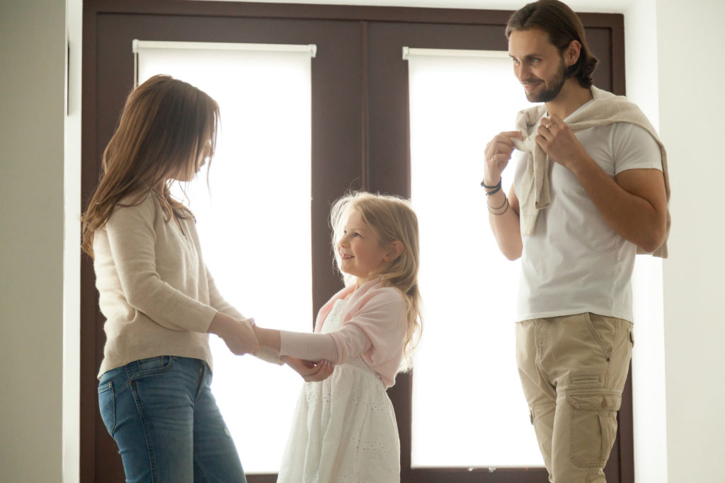 Caring mother helping little daughter dressing for walk with dad, family talking getting ready to go out standing in house hall, divorced young couple shared parenting and joint custody concept