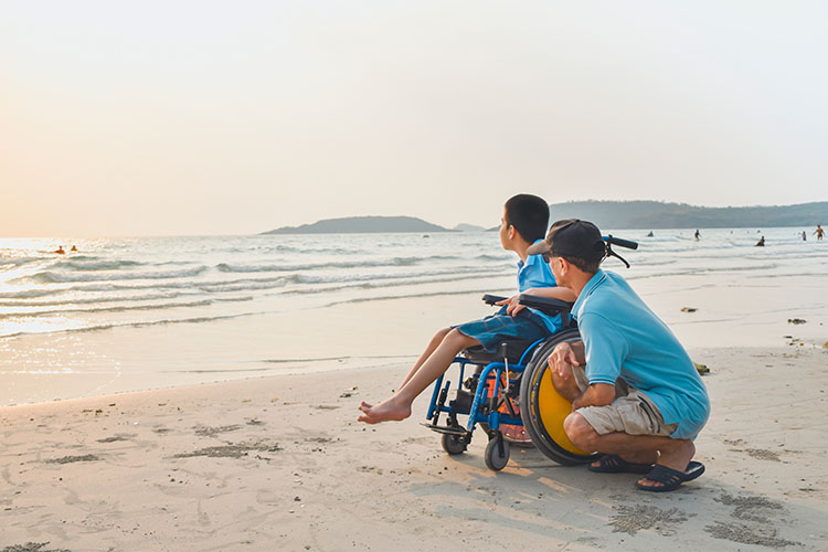 A special needs child in wheelchair and parent going at the beach