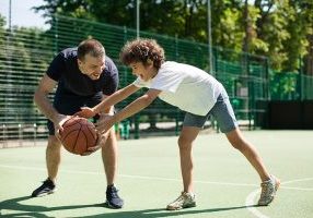 Sports Education. Full body length portrait in action of adult man and young boy playing basketball on a court, coach leading the ball and dribbling, teaching little player, spending time outdoors