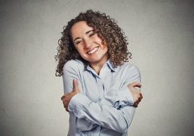 Closeup portrait confident smiling woman holding hugging herself isolated grey wall background. Positive human emotion, facial expression, feeling, reaction, situation, attitude. Love yourself concept